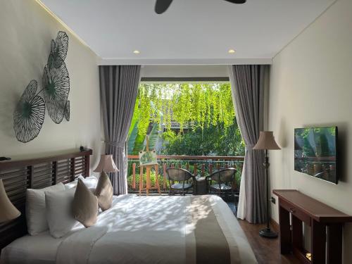 a bedroom with a large bed and a balcony at Silk Sense Hoi An River Resort - A Sustainable Destination in Hoi An