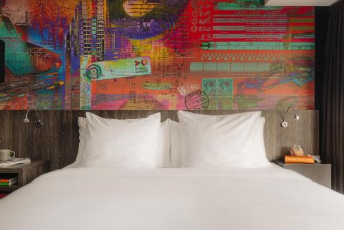 a bed with white pillows in front of a colorful wall at Leonardo Hotel Eindhoven City Center in Eindhoven