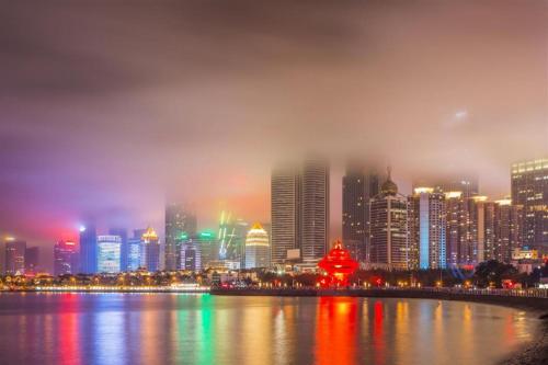 eine Skyline der Stadt in der Nacht mit einem Fluss und Gebäuden in der Unterkunft City 118 Hotel Qingdao Boardcast Tower in Qingdao