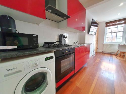 a kitchen with a washing machine and red cabinets at Hidden Leicester&Covent Garden Gem in London