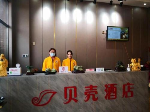 zwei Personen, die hinter einem Tisch mit Maske stehen in der Unterkunft Shell Hotel Nanyang High-Speed Railway Station Jiangying Airport Huayaocheng in Nanyang