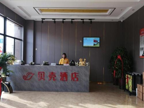 Ein Mann sitzt an der Rezeption in der Lobby. in der Unterkunft Shell Hotel Nanyang High-Speed Railway Station Jiangying Airport Huayaocheng in Nanyang