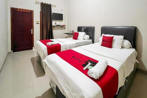 two beds in a room with red and white blankets at RedDoorz Syariah Near RSUD Dr HM Rabain in Muaraenim