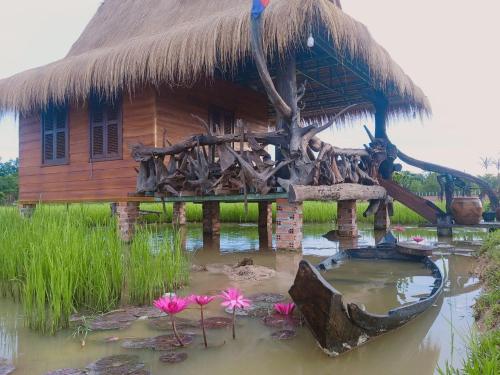 a house with a thatched roof and flowers in the water at Meta Homestay in Phumĭ Puŏk Chăs