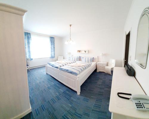 a white bedroom with a bed and a desk at Hotel-Pension Haus Hubertus in Borkum