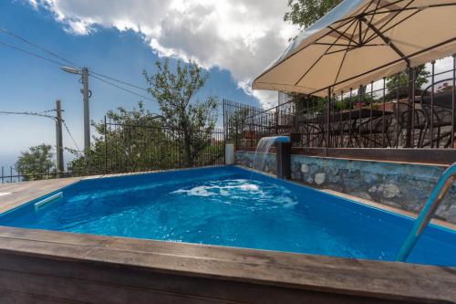 a blue swimming pool with an umbrella next to a building at Nido Degli Dei in Agerola