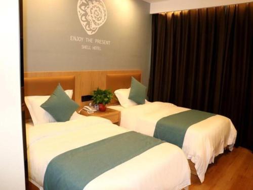 Shell Hotel Bozhou Lixin County Passenger Center في Lixin: سريرين في غرفة في الفندق مع وضع علامة على الحائط