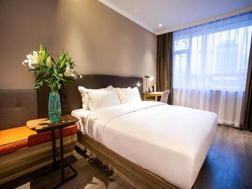 Hanting Premium Hotel Jinan Shandong University Central Campus في Licheng: غرفة نوم بسرير ابيض و مزهرية ورد