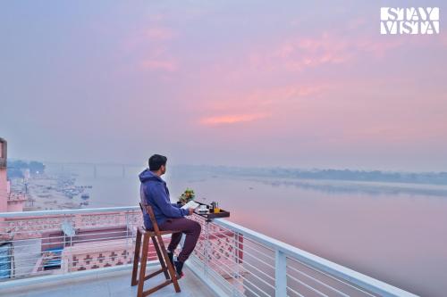 a man sitting on a chair on a bridge overlooking the water at StayVista at The Ganga House - Holy River Varanasi in Varanasi
