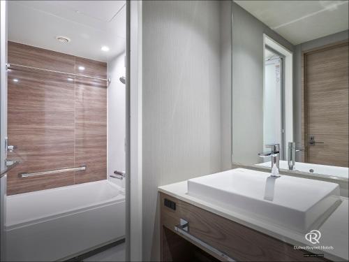 a bathroom with a white sink and a bath tub at Daiwa Roynet Hotel Osaka Sakaisuji Honmachi PREMIER in Osaka