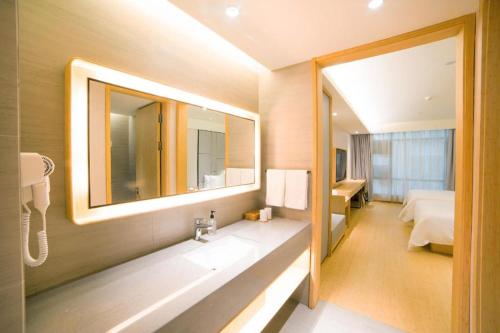 a bathroom with a sink and a mirror and a bed at Ji Hotel Guangzhou Baiyun Airport in Huadu