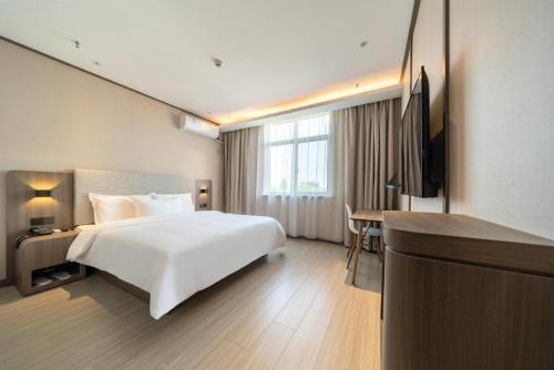 Ssu-t'uan-ts'angにあるHanting Hotel Shanghai Safari Park Nanzhu Roadの白いベッドとデスクが備わるホテルルームです。