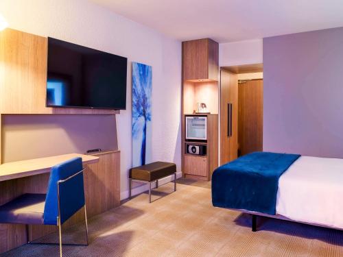 ein Hotelzimmer mit einem Bett und einem Schreibtisch mit einem TV in der Unterkunft Novotel Avignon Nord in Sorgues