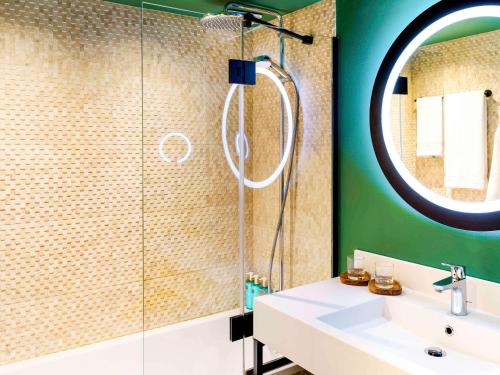 ein Bad mit einer Dusche, einem Waschbecken und einem Spiegel in der Unterkunft Novotel Avignon Nord in Sorgues