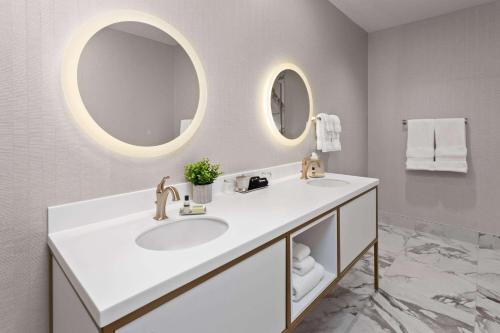 a white bathroom with a sink and two mirrors at Legacy Hotel, Trademark Collection by Wyndham in Green Bay