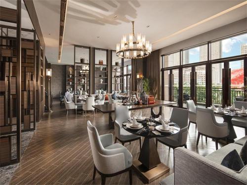 a dining room with white chairs and tables and windows at Steigenberger Hotel SUNAC Jinan in Hongjialou