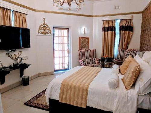 a bedroom with a large bed and two chairs at Selborne Hotel in Bulawayo