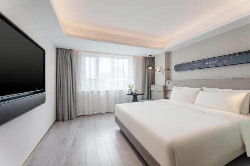 Atour Light Hotel Dalian Xinghai Plaza Xi'an Road في داليان: غرفة نوم بيضاء مع سرير كبير وتلفزيون بشاشة مسطحة