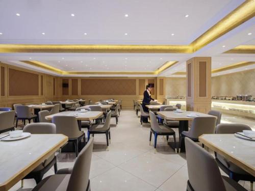 un homme debout dans une salle à manger avec des tables et des chaises dans l'établissement Vienna Hotel Shanxi Datong High-Speed Railway Dongxin International, à Shaling