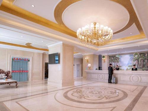 a man standing in a hotel lobby with a chandelier at Vienna Hotel Qinghai Xining Wanda Plaza in Xining