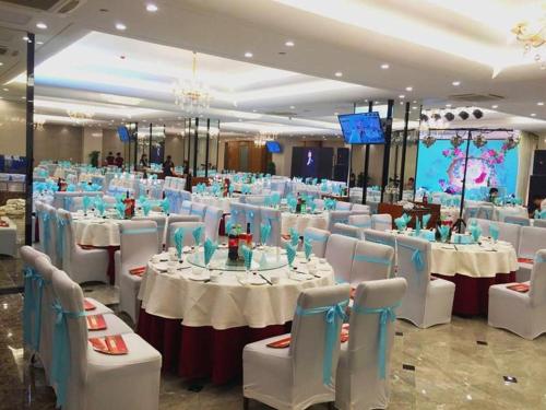 um salão de banquetes com mesas brancas e cadeiras brancas em Vienna Hotel Shandong Yantai Wanda Plaza Suochengli em Yantai