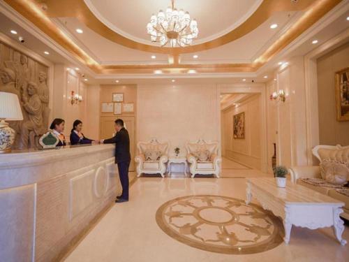 two people standing at a counter in a hotel lobby at Vienna Hotel Qinghai Yushu Tangfan Avenue in Chumda