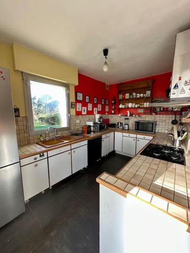 une grande cuisine avec des placards blancs et des murs rouges dans l'établissement Grande maison - Vue mer, Plage de Rospico à pied, à Névez