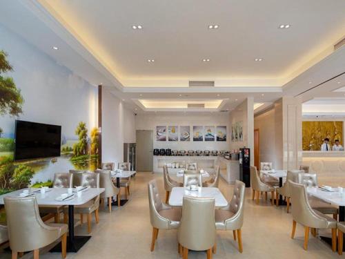 a restaurant with white tables and chairs and a television at Vienna Hotel Nanning Airport in Tanbai