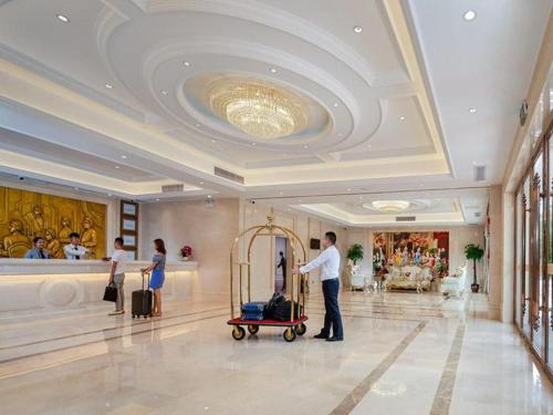 a man standing in a hotel lobby with a cart of luggage at Vienna Hotel Nanning Airport in Tanbai