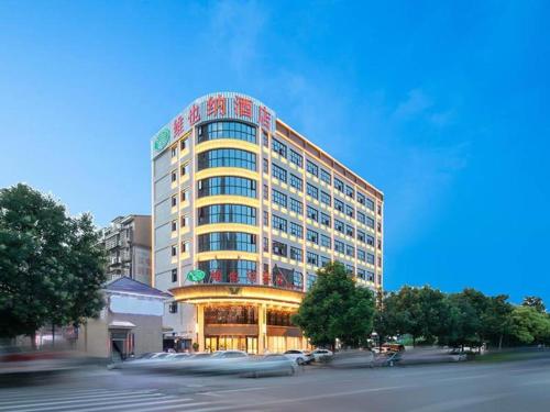岳陽的住宿－Vienna Hotel Hunan Yueyang Bubugao，一座高大的建筑,前面有汽车停放