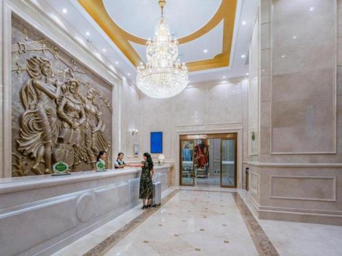 Vienna Hotel Kunming Dianzhong New District في Yanglin: امرأة تقف في بهو مع ثريا