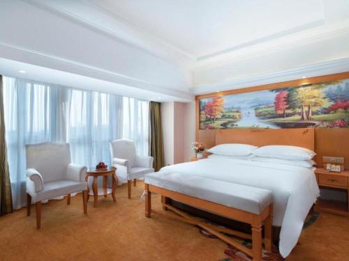 Vienna Hotel Kunming Dianzhong New District في Yanglin: غرفة نوم بسرير كبير وكرسيين