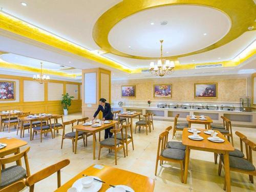 a restaurant with wooden tables and chairs and a person at Vienna Hotel Hubei Xiangyang Tang City Gulou in Xiangyang