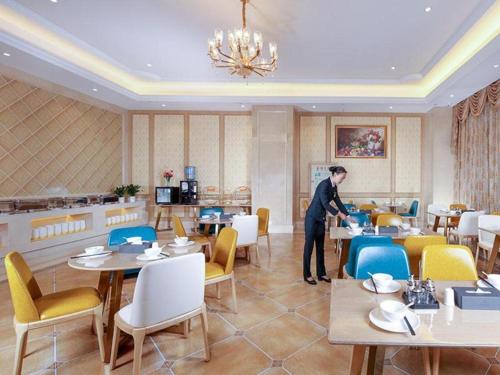 a man standing in a restaurant with tables and chairs at Vienna Hotel Baoshan Yongchang Road in Baoshan