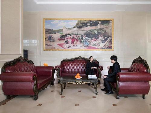 Vienna Hotel Hohhot Zhaojun Road في هوهوت: رجلان يجلسان في غرفة المعيشة بأثاث احمر