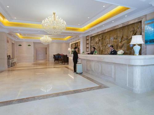 GongqingchengにあるVienna Hotel Jiangxi Jiujiang Gongqingcheng High-Speed Railway Stationのホテルロビーにスーツケースを持った女性