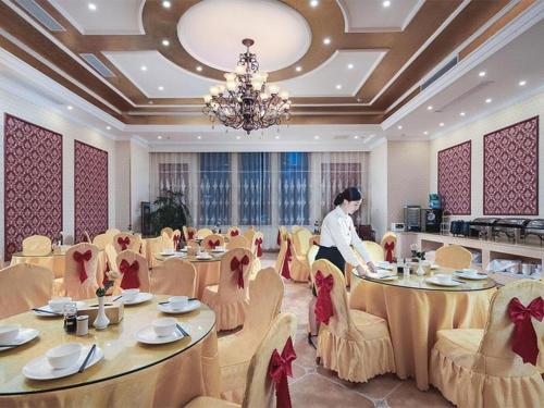 a woman standing in a dining room with tables and chairs at Vienna Hotel Jiangsu Suzhou Wujiang Bus Passenger Station in Hubin