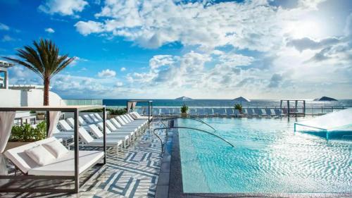 uma piscina com espreguiçadeiras brancas e o oceano em SuitesRUs At W Hotel Fort Lauderdale em Fort Lauderdale