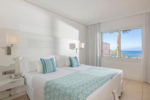 een witte slaapkamer met een groot bed en een raam bij Landmar Costa los Gigantes in Puerto de Santiago