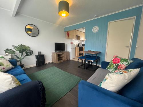 a living room with two blue couches and a kitchen at Macs Shack, Two bed Chalet on California Sands Holiday Park - Sleeps 5, pet friendly, includes FREE pool passes - plus bed linen and towels included - only 300m from the beach! in Great Yarmouth