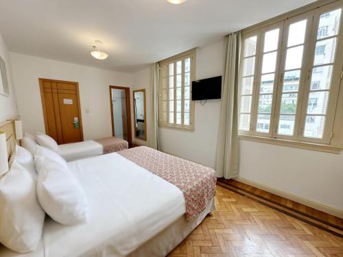 a bedroom with a large white bed and windows at Hotel Monte Alegre in Rio de Janeiro