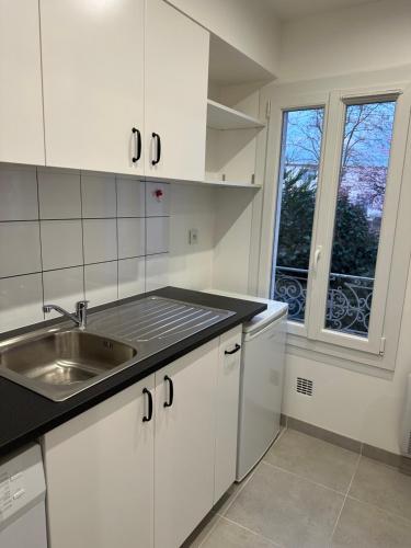 une cuisine avec des armoires blanches, un évier et une fenêtre dans l'établissement Paris - Drancy, à Drancy