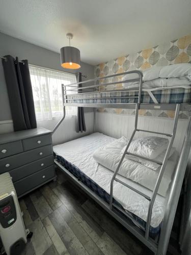 a bedroom with two bunk beds and a lamp at 170, Two bed Chalet on Sunbeach Holiday Park - Sleeps 5, pet friendly, bed linen and towels included plus Wi-Fi included - only 300m from the beach! in Scratby