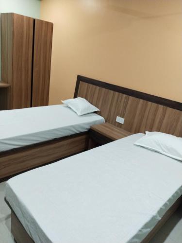 two beds in a hotel room with white sheets at Hotel Jyoti in Madhubani
