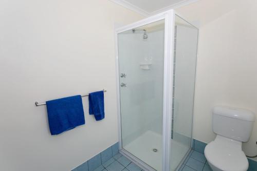 a bathroom with a shower with a toilet and blue towels at Dolphin Lodge Albany - Self Contained Apartments at Middleton Beach in Albany