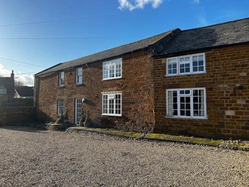 a brick house with white windows on a gravel driveway at Quail in Lyddington