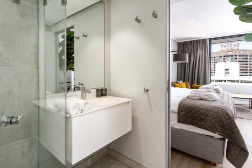een badkamer met een wastafel, een bed en een douche bij Cape Town Bree Street 27th Floor Studio Apt Views in Kaapstad