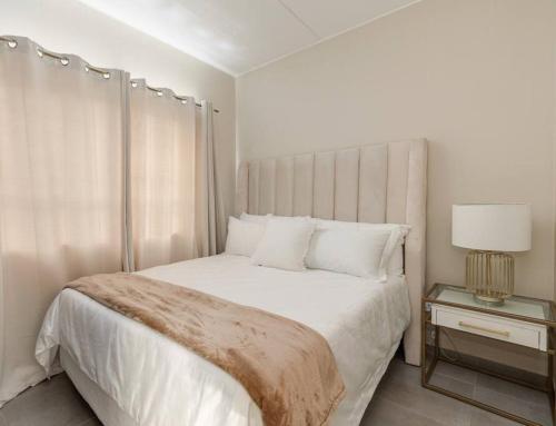 a white bedroom with a large bed and a lamp at Waterfall Ridge - Retreat in the heart of Midrand in Midrand