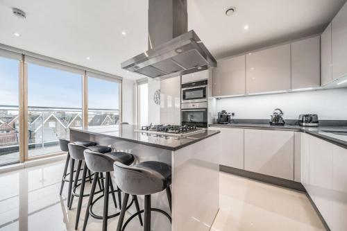 a kitchen with white cabinets and a counter with bar stools at Amazing One bedroom Penthouse in Wimbledon in London
