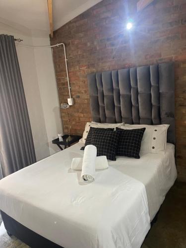 1 dormitorio con 1 cama blanca grande y pared de ladrillo en Dream Abodes at Cozy Craftmans Ship, Maboneng en Johannesburgo
